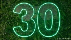 Green neon number "30" illuminated on a leafy background.
