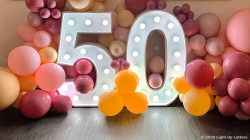 A large illuminated "50" sign surrounded by colorful balloons in shades of pink, orange, and yellow.