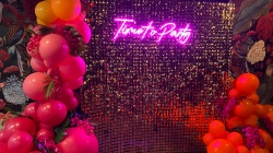 Neon "Time to Party" sign on a gold sequined backdrop with colorful balloon decorations on the sides.