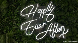 Neon sign reading "Happily Ever After" against a backdrop of green foliage.