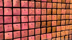 A wall of shimmering, reflective, square pink tiles arranged in a grid pattern.