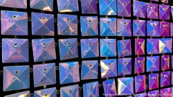A wall of reflective, iridescent square panels with a diamond pattern arranged in rows and columns.