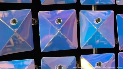 Close-up of shiny, square mirrored tiles arranged in a grid, reflecting various shades of blue and purple.