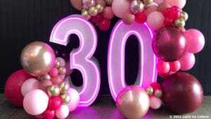 Neon number "30" decorated with an assortment of pink, red, and gold balloons.
