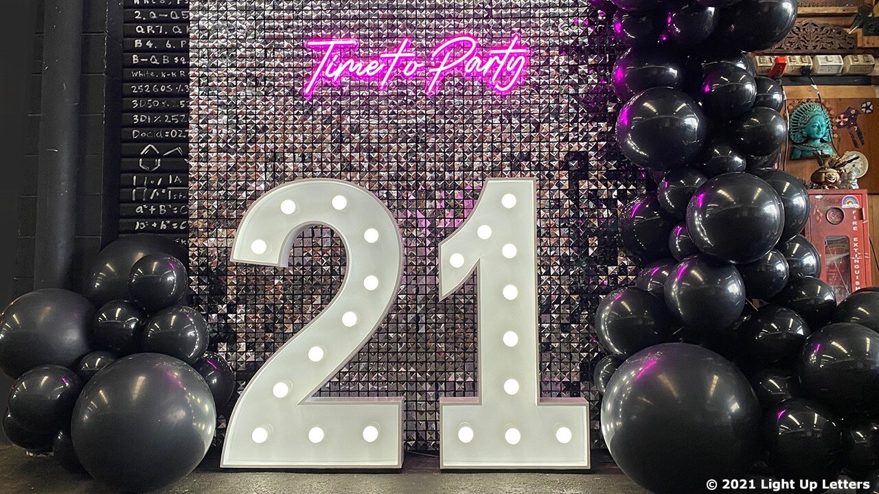 Decor with large illuminated numbers "21," black balloons, and a sequined backdrop with a neon sign reading "Time to Party.