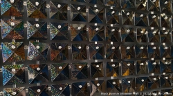 Wall display of triangular, reflective solar panels arranged in a grid pattern, with each panel displaying varying degrees of illumination.