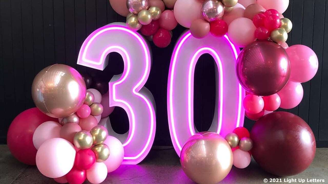 Neon number "30" decorated with an assortment of pink, red, and gold balloons.