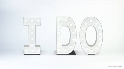 White marquee letters spelling "I DO" with lights, set against a plain light background.
