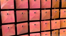 Close-up of a wall display featuring rows of square, reflective orange tiles with a small circular fixture in the center of each tile.