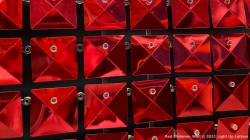 A grid of shiny red metallic square tiles, each with a small central attachment, creating a reflective pattern.