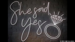 Neon sign reads "She said yes" with a diamond ring illustration on a dark background.