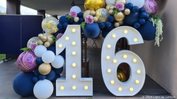 Large illuminated numbers "16" surrounded by blue, gold, and pink balloons with floral decorations.