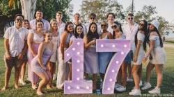 A group of people posing outdoors with large, illuminated numbers "17" on a grassy area.