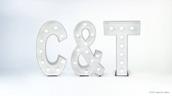 Giant marquee letters "C & T" stand on a white background, each illuminated with round bulbs.