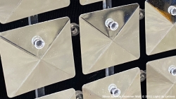 Close-up of metallic, square-shaped panels with a reflective surface, each featuring a central protrusion, placed against a dark background.