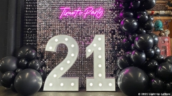 Large illuminated "21" surrounded by black balloons, with a "Time to Party" neon sign above.